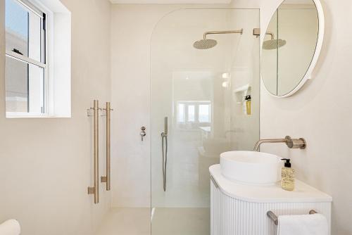 a white bathroom with a sink and a mirror at Beachfront 1 Bed across from iconic BONDI BEACH in Sydney