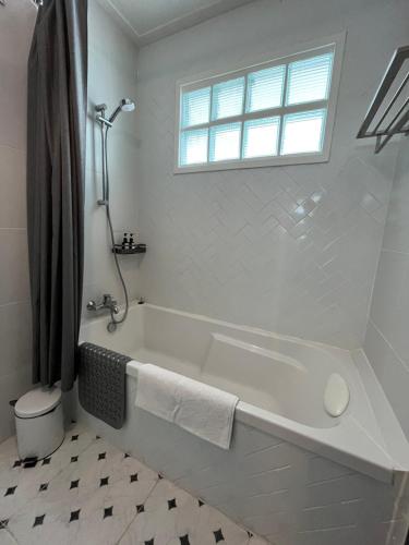 a white bathroom with a tub and a window at Baan Debtida in Bangkok