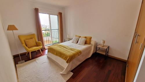 a bedroom with a bed and a chair and a window at Casa Nóbrega in Caniço