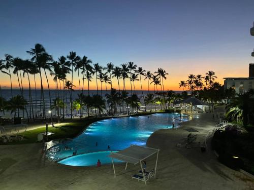 - une piscine avec des palmiers et l'océan au coucher du soleil dans l'établissement Beachfront Apartment Marbella, Juandolio, à Villas del Mar
