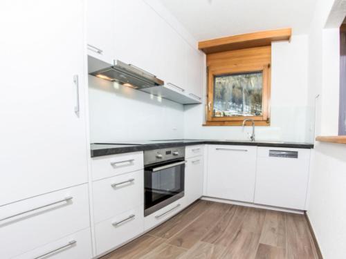a kitchen with white cabinets and a wooden floor at Apartment Metropol B by Interhome in Grächen