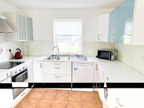 une cuisine blanche avec un évier et un micro-ondes dans l'établissement Holiday Home Brittas Bay Holiday Village No 7 by Interhome, à Brittas Bay