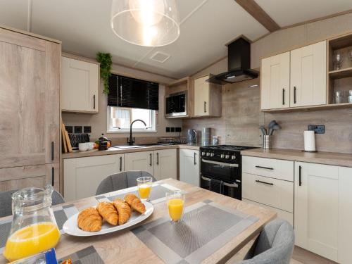 a kitchen with a table with a plate of croissants and orange juice at Chalet Lodge 15 by Interhome in Boat of Garten