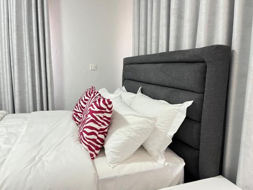 a bed with white pillows and a gray headboard at Beauty Blender Homes - The Monotone House in Lilongwe