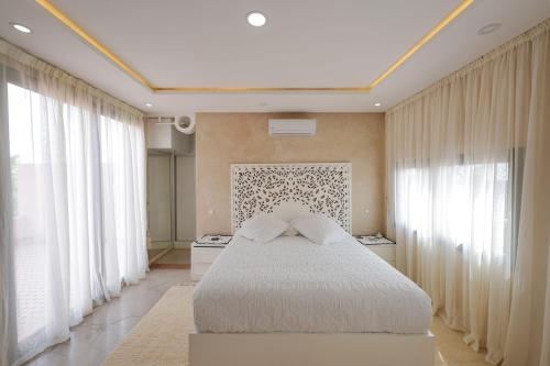 a bedroom with a bed with white sheets and windows at Villa Dar El Gharrabia in Amezrou