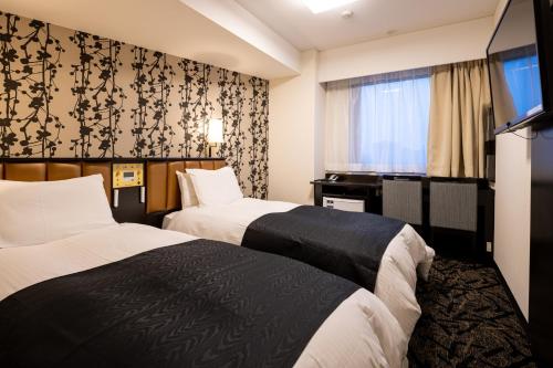 two beds in a hotel room with a flat screen tv at APA Hotel Koriyama Ekimae in Koriyama