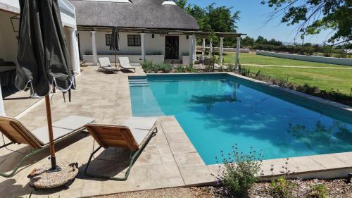 a swimming pool with chairs and an umbrella at Villa Canetsfontein in Wellington