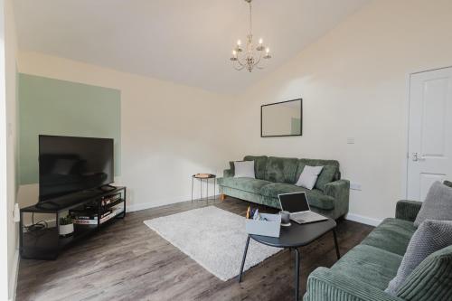 a living room with a green couch and a tv at NEW! Large 5BR 3BA Home Leamington Spa Driveway Parking WI-FI in Leamington Spa