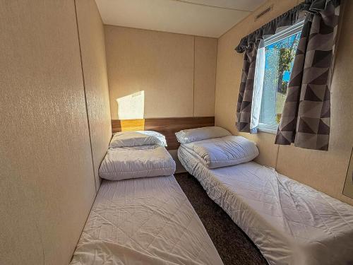 duas camas em um pequeno quarto com janela em Lovely Caravan For Hire At Manor Park In Hunstanton Ref 23053B em Hunstanton