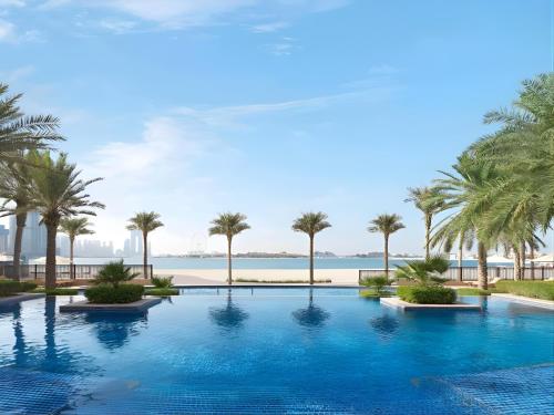 a pool with palm trees and the ocean in the background at Dimorelux l Club Vista Mare l Five Palm Jumeirah in Dubai