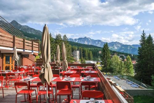 a restaurant with tables and chairs with mountains in the background at Belambra Clubs Arc 1800 - Hôtel Du Golf in Arc 1800