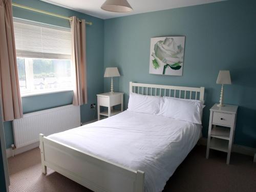 a bedroom with a white bed with blue walls and a window at Holiday Home Glen Ard HH No 1 by Interhome in Dunmore East