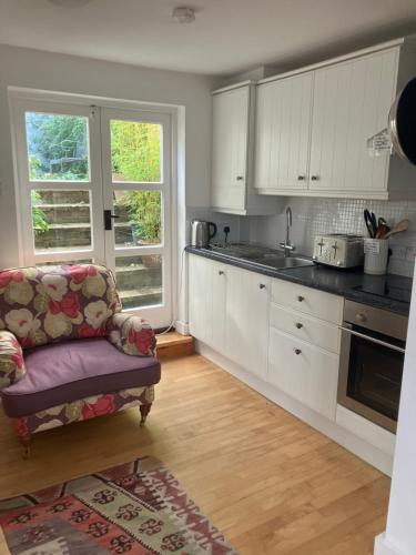a kitchen with white cabinets and a chair in a room at Riverside country cottage in Newhaven