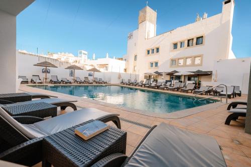 a swimming pool with chairs and a building at Hotel Carvoeiro Plaza in Carvoeiro