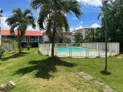 une clôture avec un palmier à côté d'une piscine dans l'établissement Studio accueillant aux Trois-Îlets, 30 m², piscine partagée, à Lazaret
