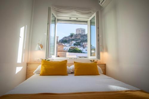 a bed with yellow pillows in a room with a window at Babel 11 Centro in Vélez de Benaudalla