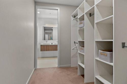 a walk in closet with white shelves and a mirror at Premium Coastal Abode with Parking Near Beach in Okura