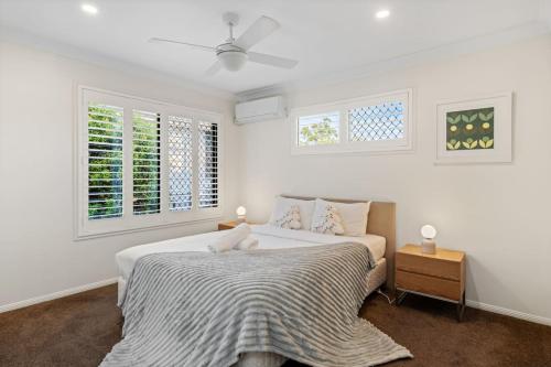 a white bedroom with a bed and two windows at Tranquil 4BR Home Near Parks Shops and Nature Trails in Cornubia Park