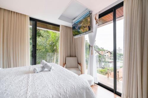 a bedroom with a white bed and a large window at Casa Atalaia 550m Praia c/ Hidro by Achei Camboriú in Praia Brava