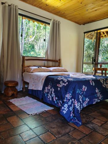 a bedroom with a bed with a blue comforter and two windows at Chalés Isa e Ana in Itatiaia