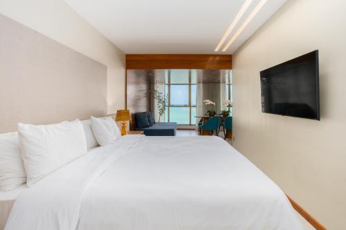 Schlafzimmer mit einem weißen Bett und einem Flachbild-TV in der Unterkunft Urban - Beira Mar Boa Viagem in Recife