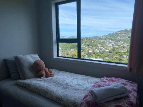 a teddy bear sitting on a bed in front of a window at Relaxing rooms with mountain views, close to ferry in Wellington