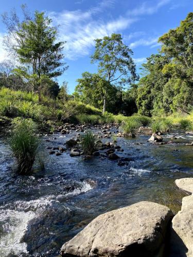 a river with rocks and trees in the background at Tallaringa Views in Alstonville