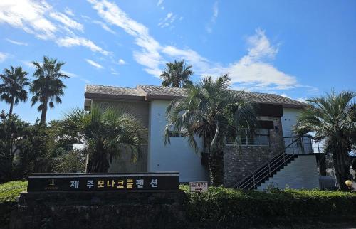 a house with palm trees in front of it at Monaco Pool Pension in Seogwipo