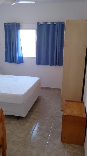 a bedroom with a bed and a window with blue curtains at Praia, Laser, Comércio in Praia Grande