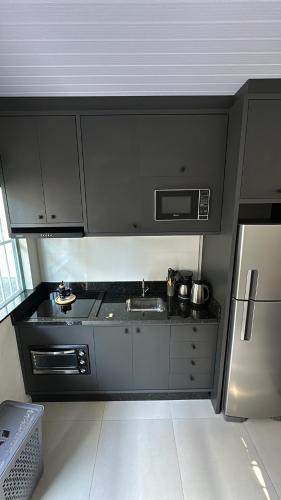 cocina con armarios negros y nevera de acero inoxidable en Casa em Içara Prox Criciúma, en Içara