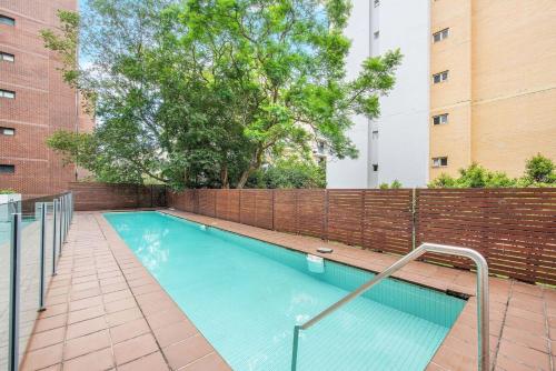 a swimming pool with a fence and a brick wall at Entire 2bed New Apartment in Waitara