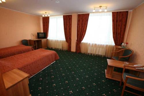 ペルヴォウラリスクにあるHotel Malahitのベッド2台、デスク、テレビが備わるホテルルームです。