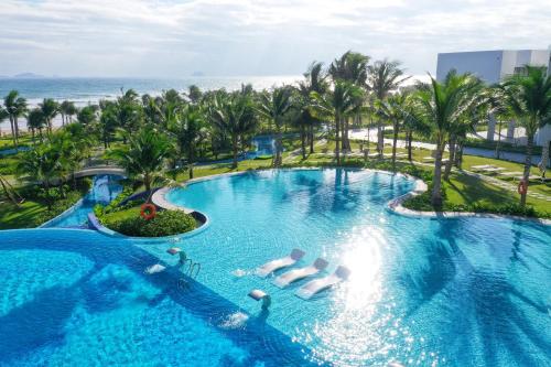 an infinity pool at a resort with palm trees and the ocean at The Light Arena Ocean Tower in Cam Ranh International Airport