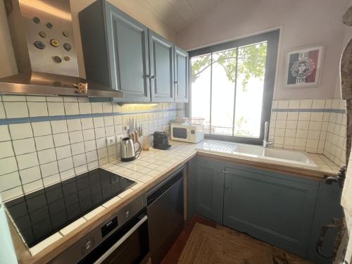 eine Küche mit blauen Schränken, einem Waschbecken und einem Fenster in der Unterkunft Maison de la Beureliere in Sainte-Marie-de-Ré