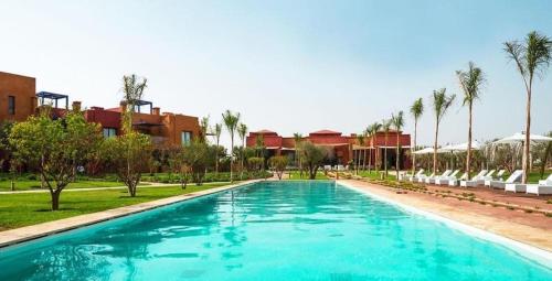 a large swimming pool with chairs and palm trees at Appartement de charme au Vizir Resort in Dar Caïd Layadi