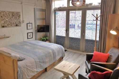 a bedroom with a bed and a chair and windows at Studio 't Krekeltje in Westkapelle