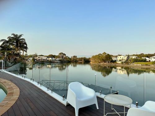 a deck with chairs and tables and a body of water at Spacious waterfront home with pontoon, pool, BBQ in Kawana Waters