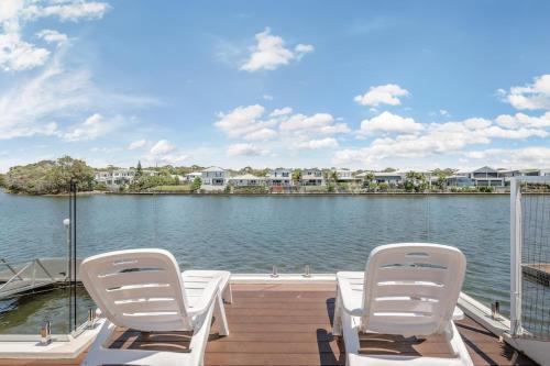 dos sillas blancas sentadas en un muelle junto al agua en Spacious waterfront home with pontoon, pool, BBQ, en Kawana Waters