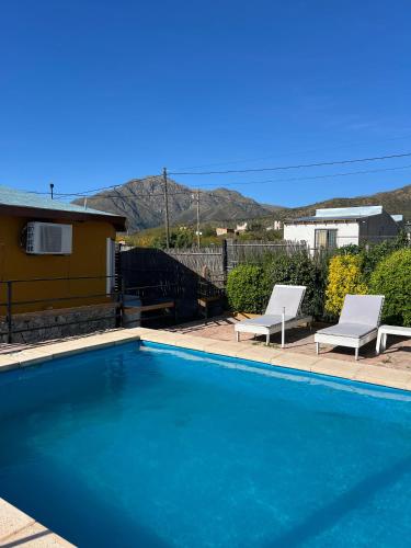 a swimming pool with two white chairs next to a house at Cabaña Paz in Capilla del Monte