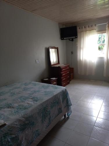 ein Schlafzimmer mit einem Bett, einer Kommode und einem Fernseher in der Unterkunft Casa da Marina in Três Coroas