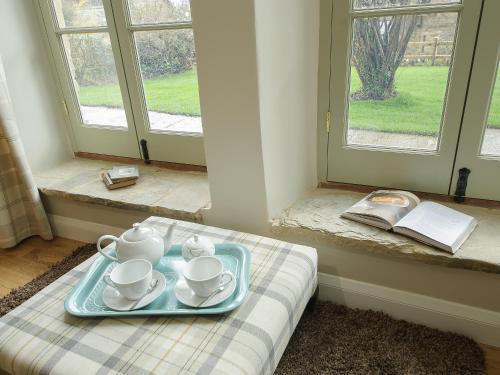 un plateau bleu avec des tasses à thé et des soucoupes sur un lit avec des fenêtres dans l'établissement Holliers Cottage, à Ledwell
