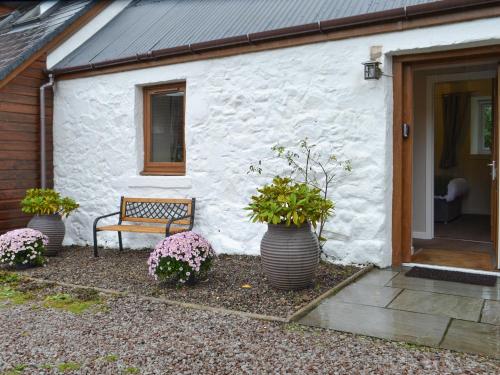eine Bank vor einem weißen Gebäude mit Topfpflanzen in der Unterkunft Blackmill Cottages No 2 in Taynuilt