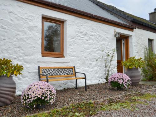 eine Bank vor einem weißen Gebäude mit Blumen in der Unterkunft Blackmill Cottages No 2 in Taynuilt