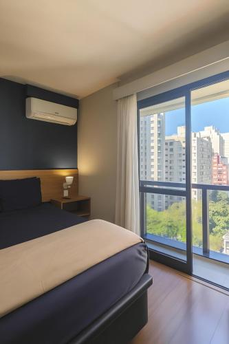 a bedroom with a bed and a large window at BOOK A FLAT Jardins São Paulo in São Paulo