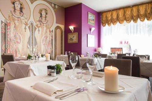 ein Esszimmer mit weißen Tischen, Kerzen und lila Wänden in der Unterkunft The Originals City Hotel de l Ange Guebwiller in Guebwiller