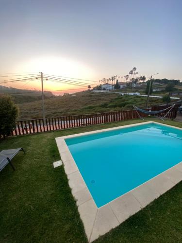 a blue swimming pool in the grass with the sunset at Like a Local Guest House in Ericeira