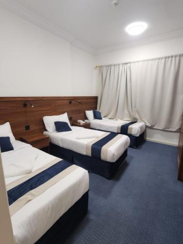 a hotel room with three beds and a window at فندق اصول الجوهرة بالعزيزية توصيل مجاني الى الحرم Asoul Al Jawhara Al Azizia Free Shuttle Service in Al ‘Azīzīyah
