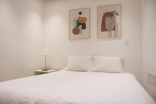 a bedroom with a white bed with two pictures on the wall at Casa de Nini in Santo Domingo