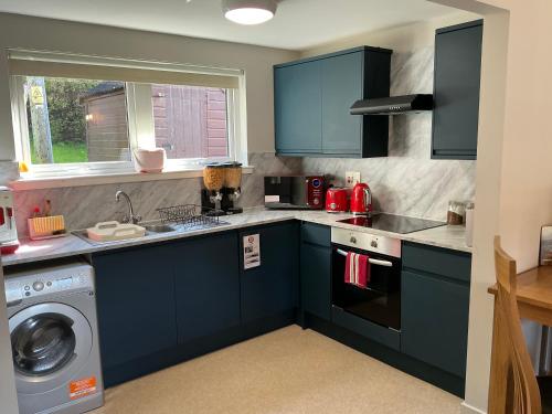a kitchen with blue cabinets and a washing machine at Conaglen, one bedroom apartment with stunning views. in Fort William