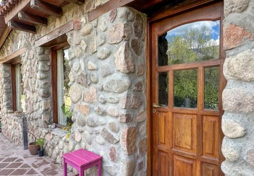 a stone house with a wooden door and a pink stool at Casa de piedra con jardin y pileta - privada in Los Hornillos